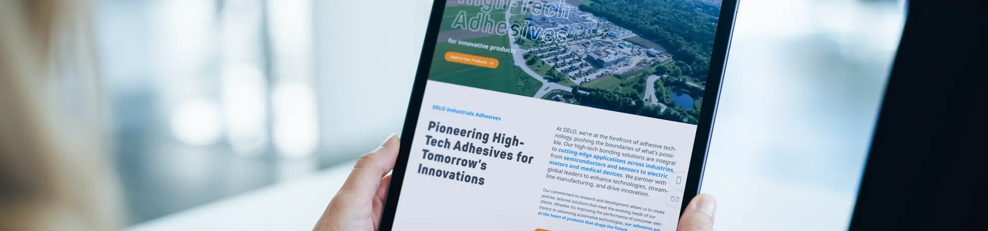 Tablet mit DELO-Website für Hightech-Klebstoffe, auf der innovative Lösungen für morgen vorgestellt werden. Person in weißem Pullover hält das Gerät vor einen Laptop. Fokus auf wegweisende Klebstofftechnologie für zukünftige Anwendungen. SEO-optimierte Darstellung der DELO-Kompetenz und der globalen Präsenz im Bereich Advanced Adhesives.